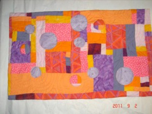 Orange, purple, pink quilt with circle cuts backed by dotted swiss