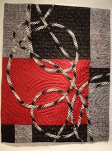 Full quilt ,red black and biasis strip cirlcleing across the surface