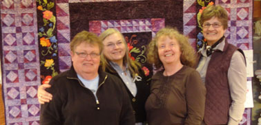 All four of us in front of a raffel quilt 